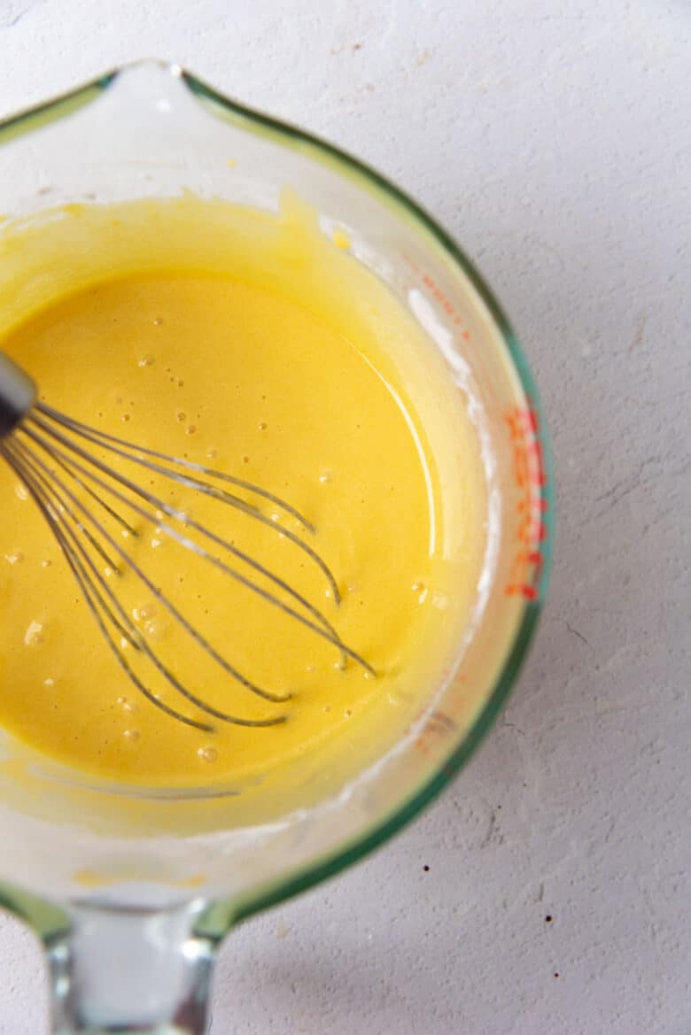 Pale yellow, smooth egg yolk mixture with a whisk inside, after being whisked.