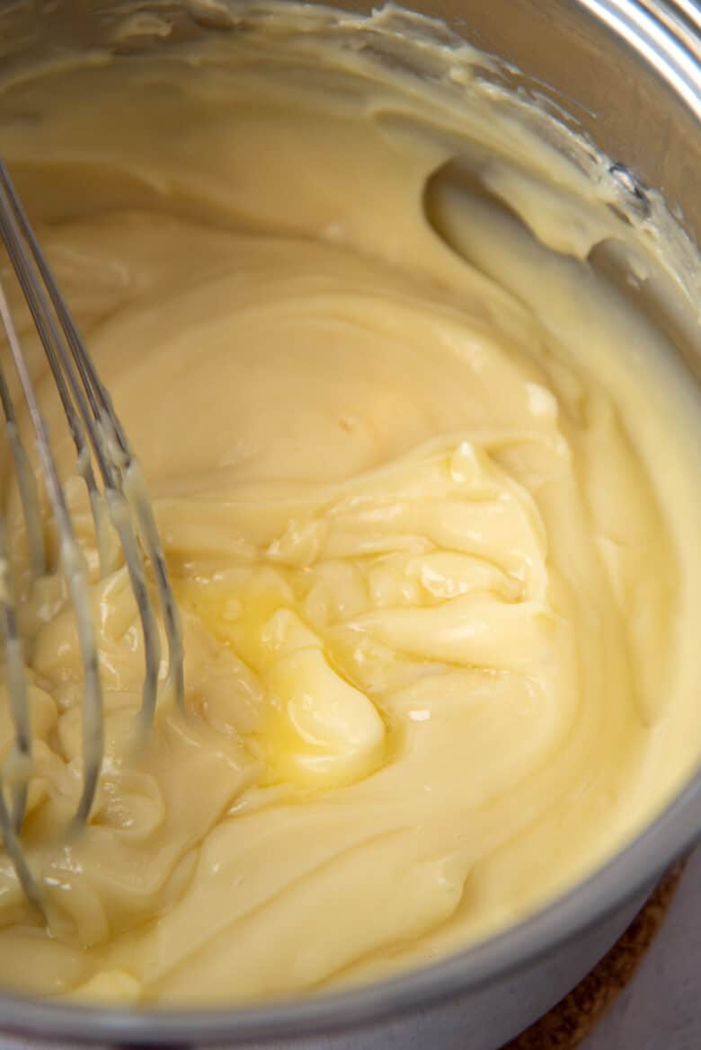 A close up of whisked pastry cream mix, with partially melted butter and a whisk in the pot.
