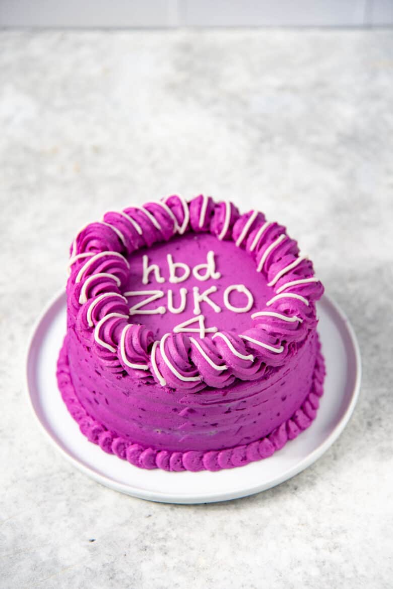 A meatloaf dog cake with a naturally dyed purple sweet potato frosting that is dog friendly, serve on a white plate with the lettering HPD Zuko" on top.