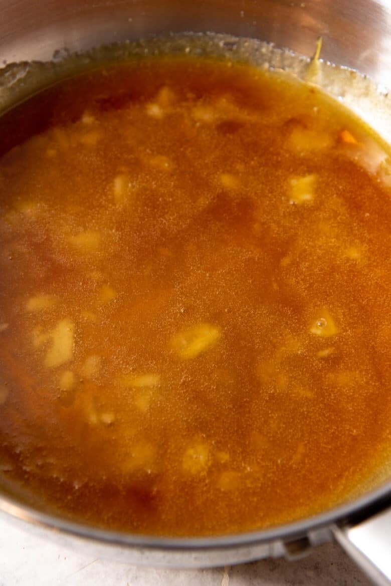 Golden brown dry caramel in a stainless steel pan, with fewer sugar lumps undissolved in the caramel.