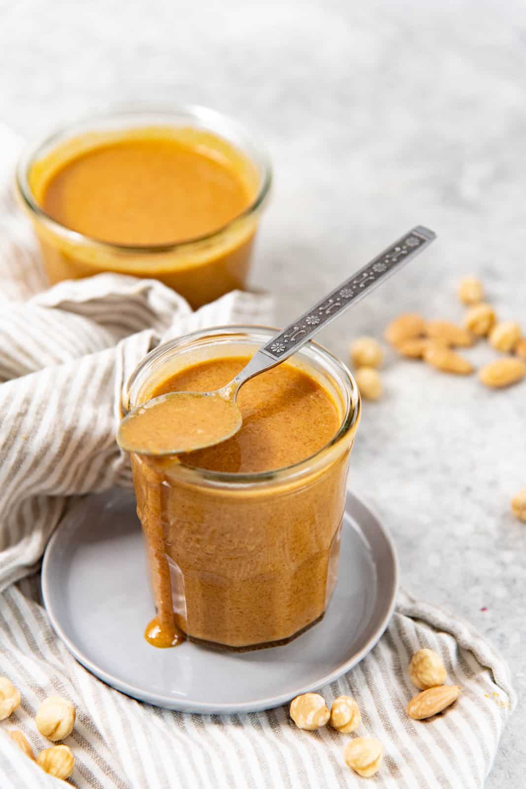 Praline paste in a tall glass jar, with a praline paste filled spoon balanced on top of the glass jar.