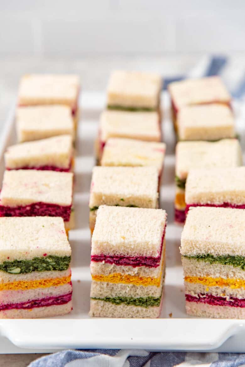 Ribbon sandwiches cut into mini squares, placed on a white platter.