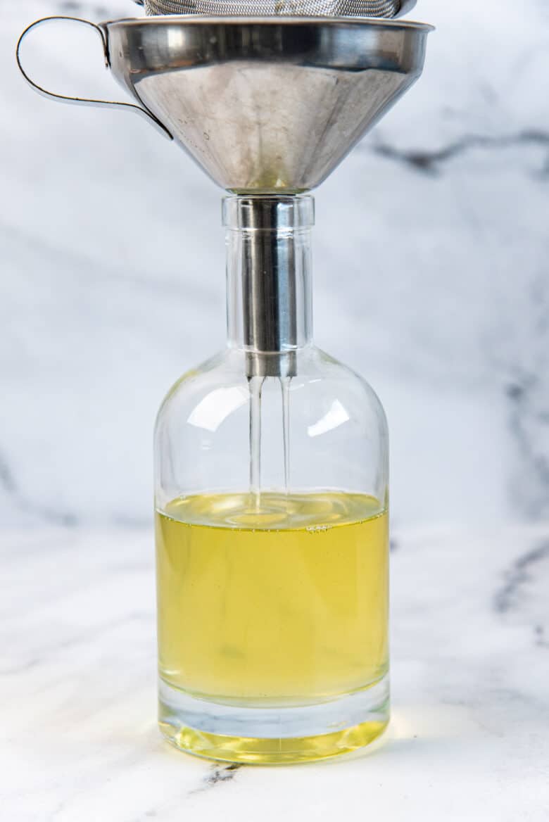 A green tinged simple syrup being poured into a glass bottle through a funnel.