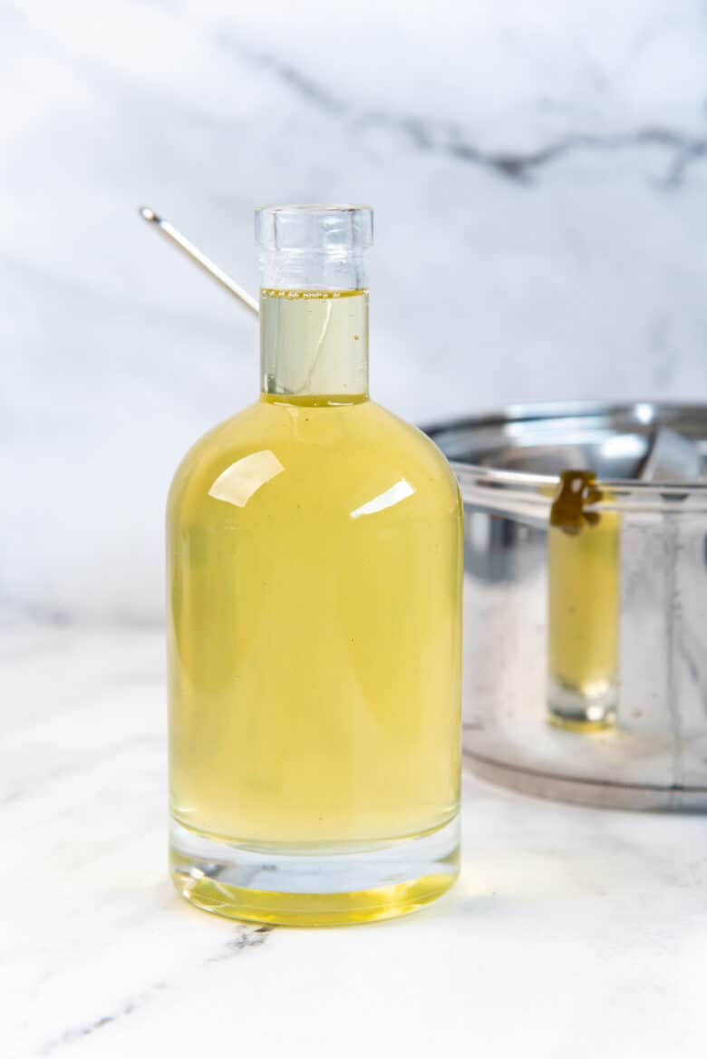 A glass bottle filled with a green tinged simple syrup next to the saucepan.