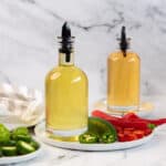 Square image of jalapeno simple syrup and red chili simple syrup in two separate bottles.