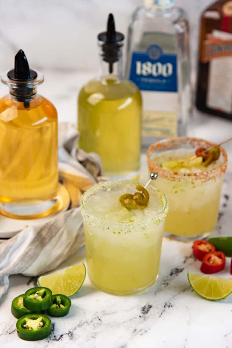 An image of spiced margarita, with the spicy simple syrup and margarita ingredients in the background.