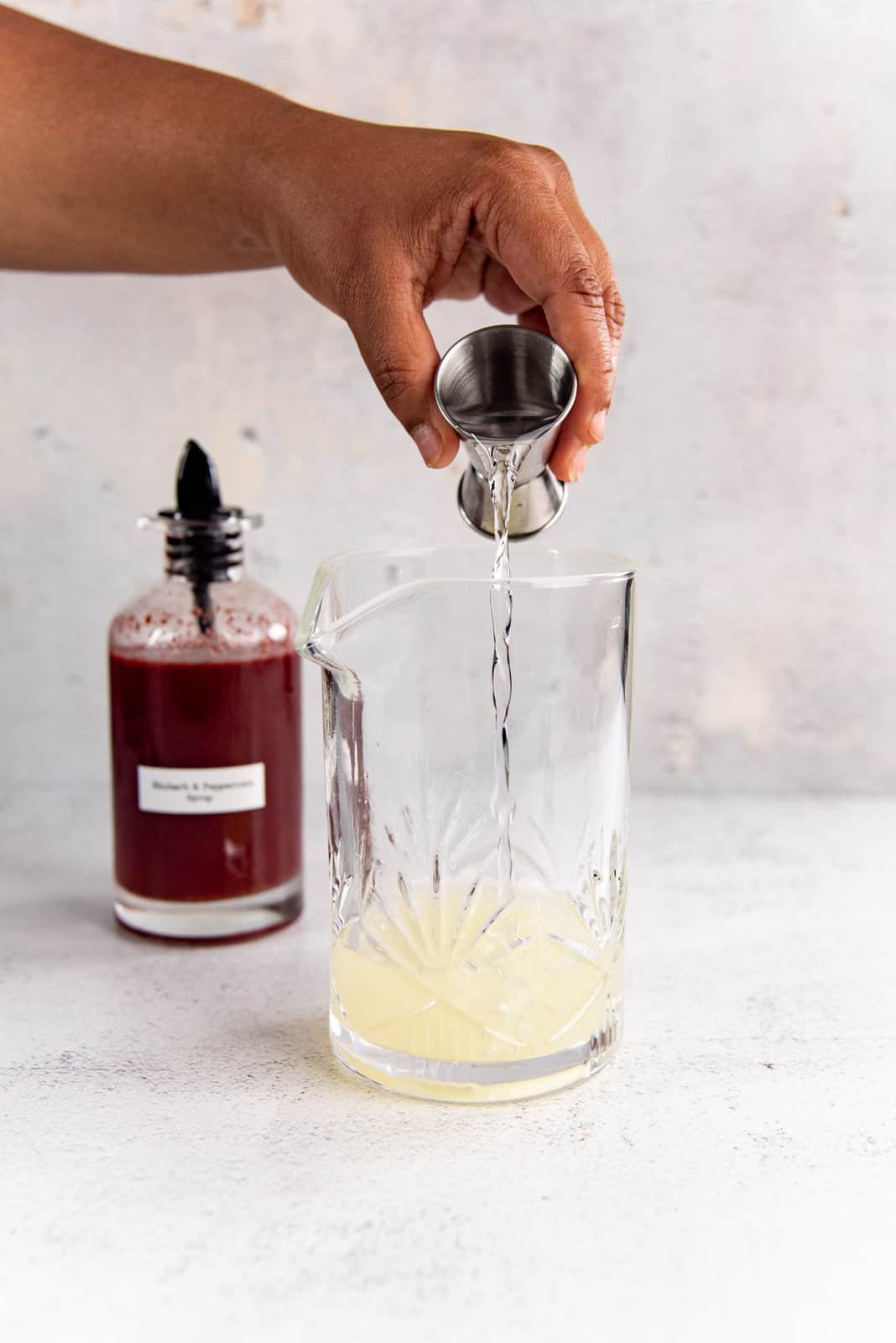 Pouring a clear liquid that is tequila into a glass cocktail shaker.