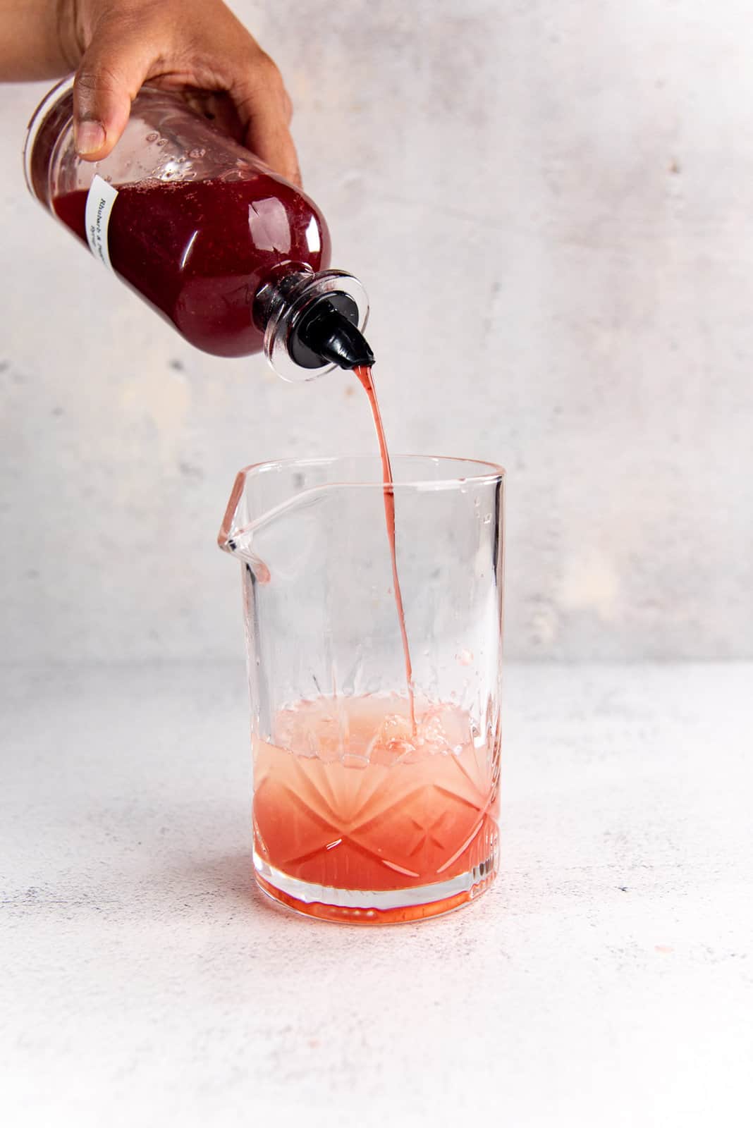 Pouring the rhubarb syrup from the syrup bottle into the glass cocktail shaker.