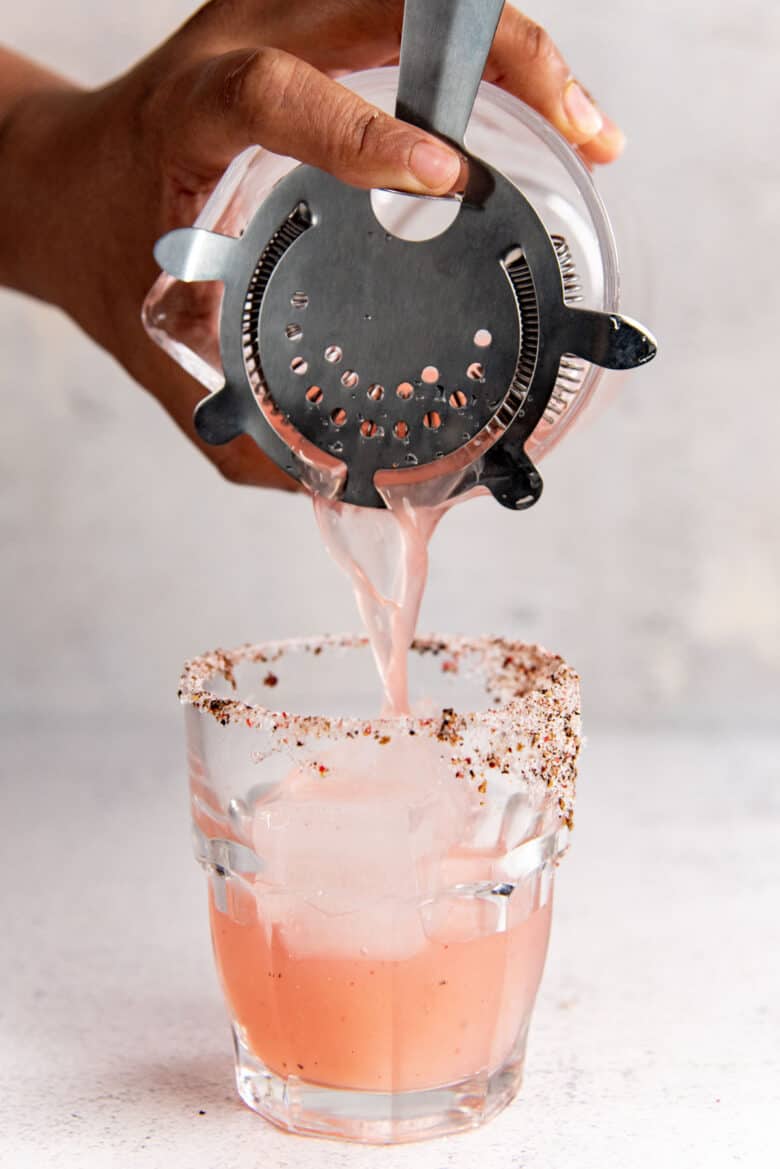 The rhubarb cocktail being poured into the glass through a strainer on the cocktail shaker.