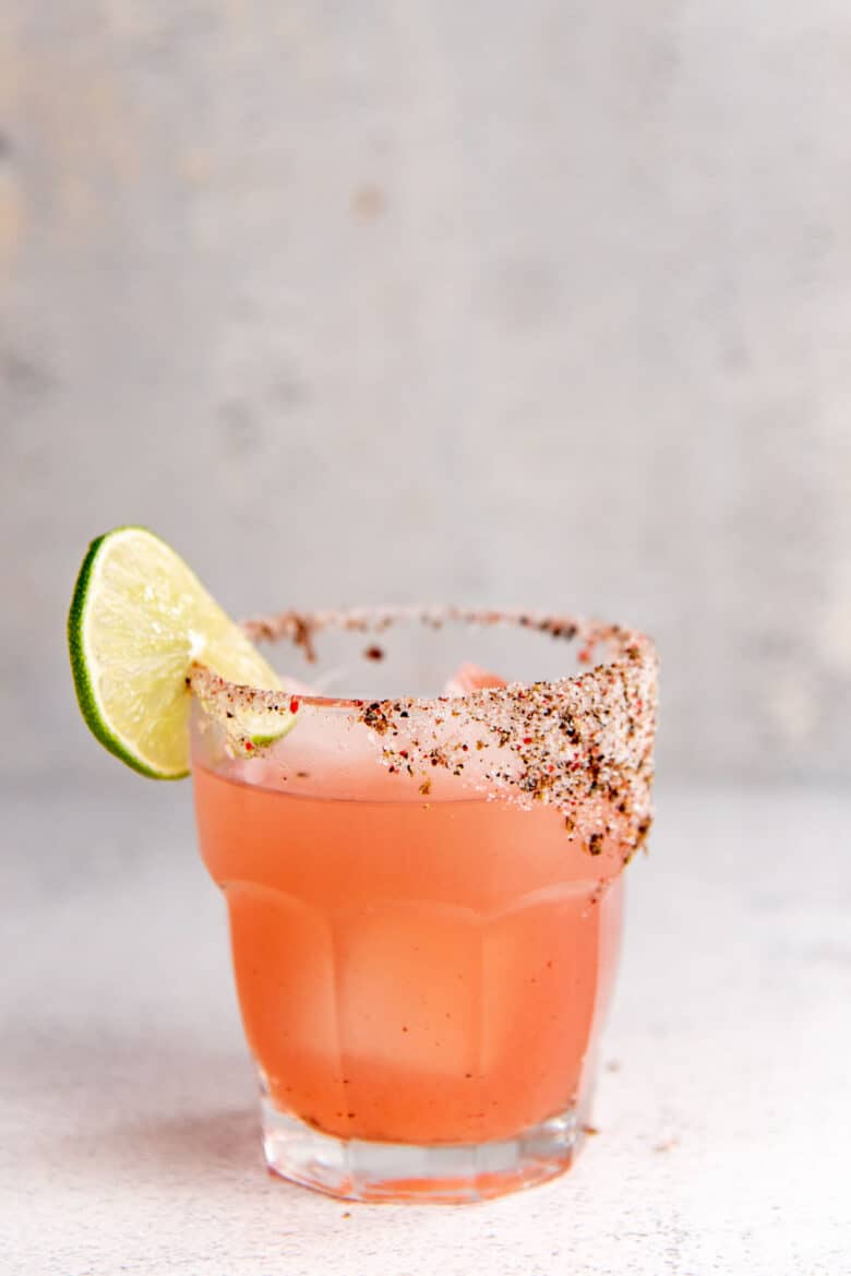 A close up of the glass of rhubarb margarita with a pepper and salt rim and lime garnish.