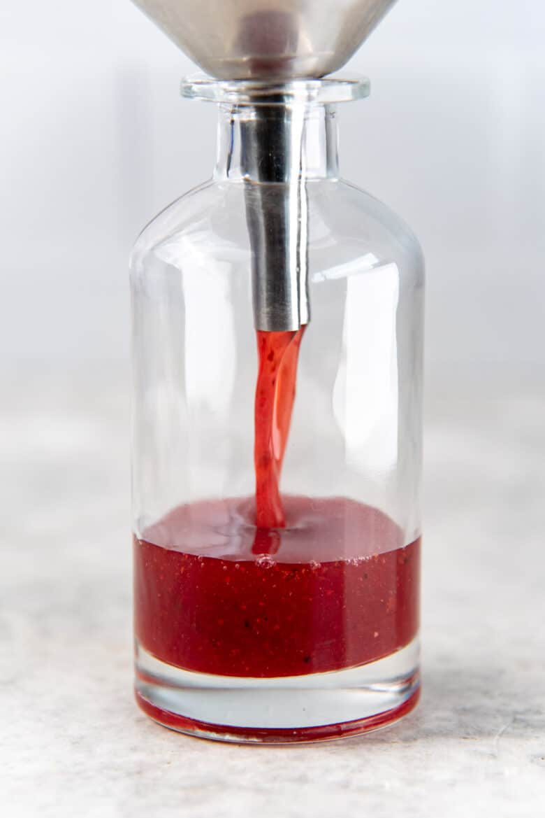 A glass bottle being filled with rhubarb syrup through a funnel