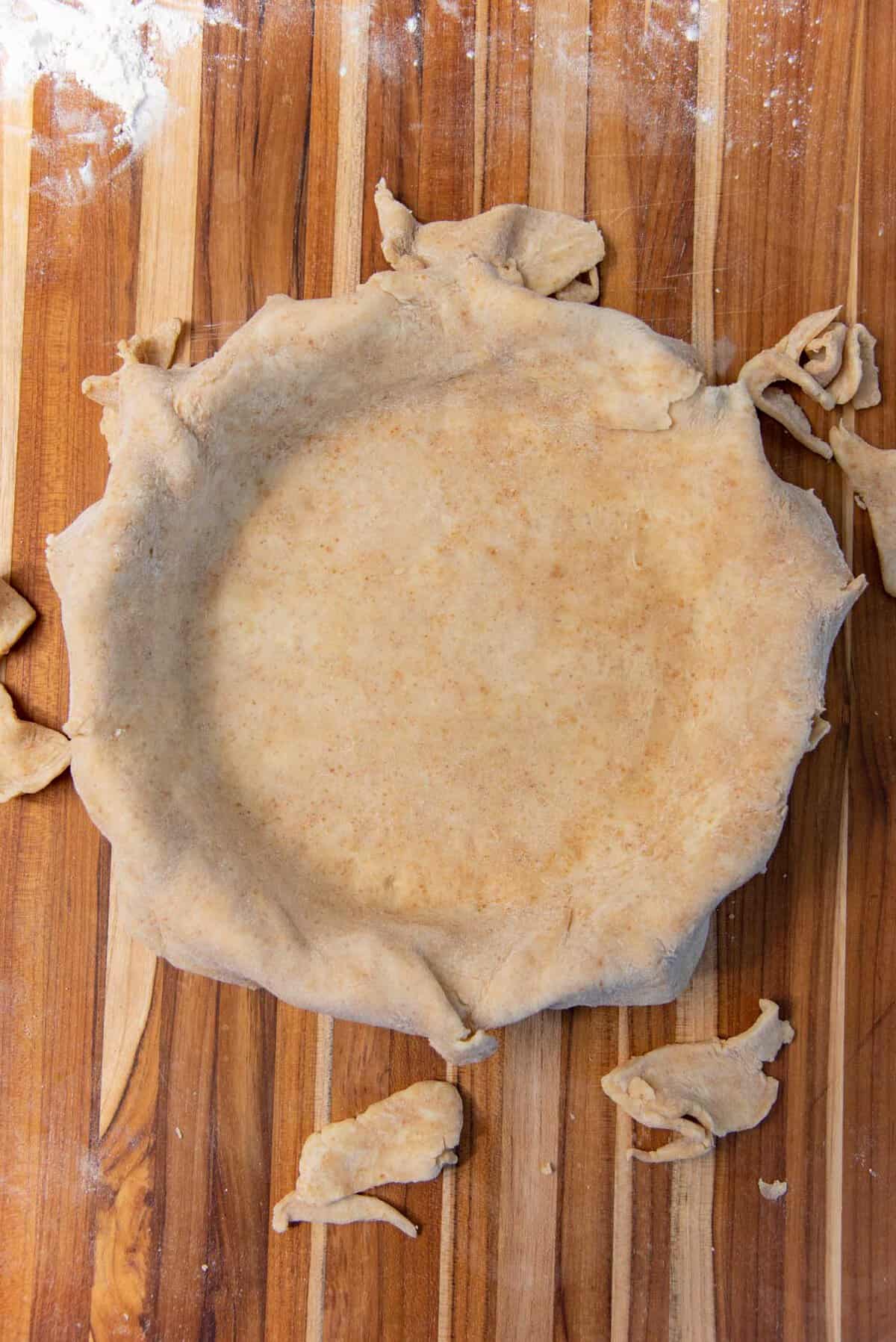 The edges of the pie crust trimmed inside a pie plate.