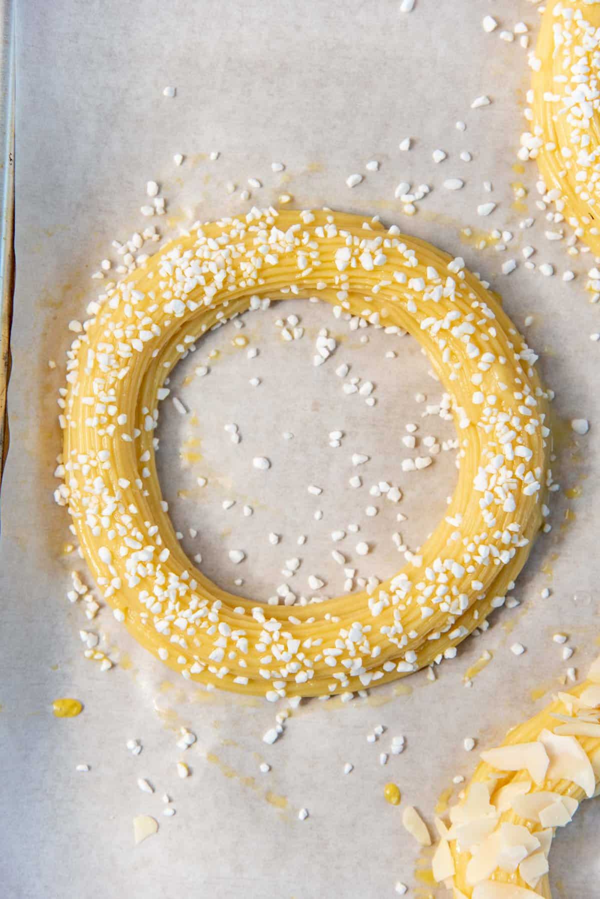 Small pearl sugar pieces sprinkled over the egg washes choux pastry rings.