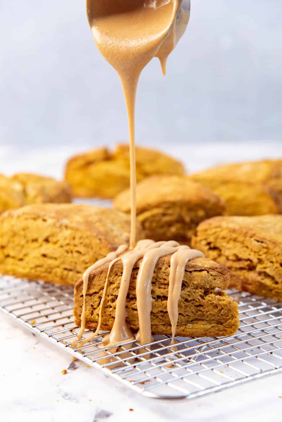 A coffee glaze being drizzled over a pumpkin wedge scone places on a wire rack.