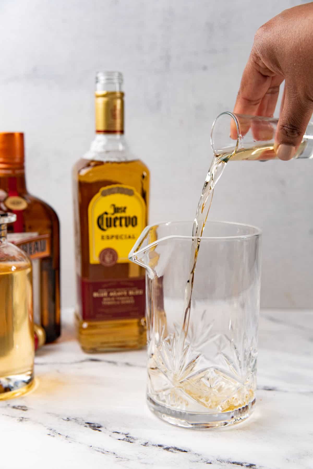 Pouring tequila into the cocktail mixing glass to make spicy margarita.