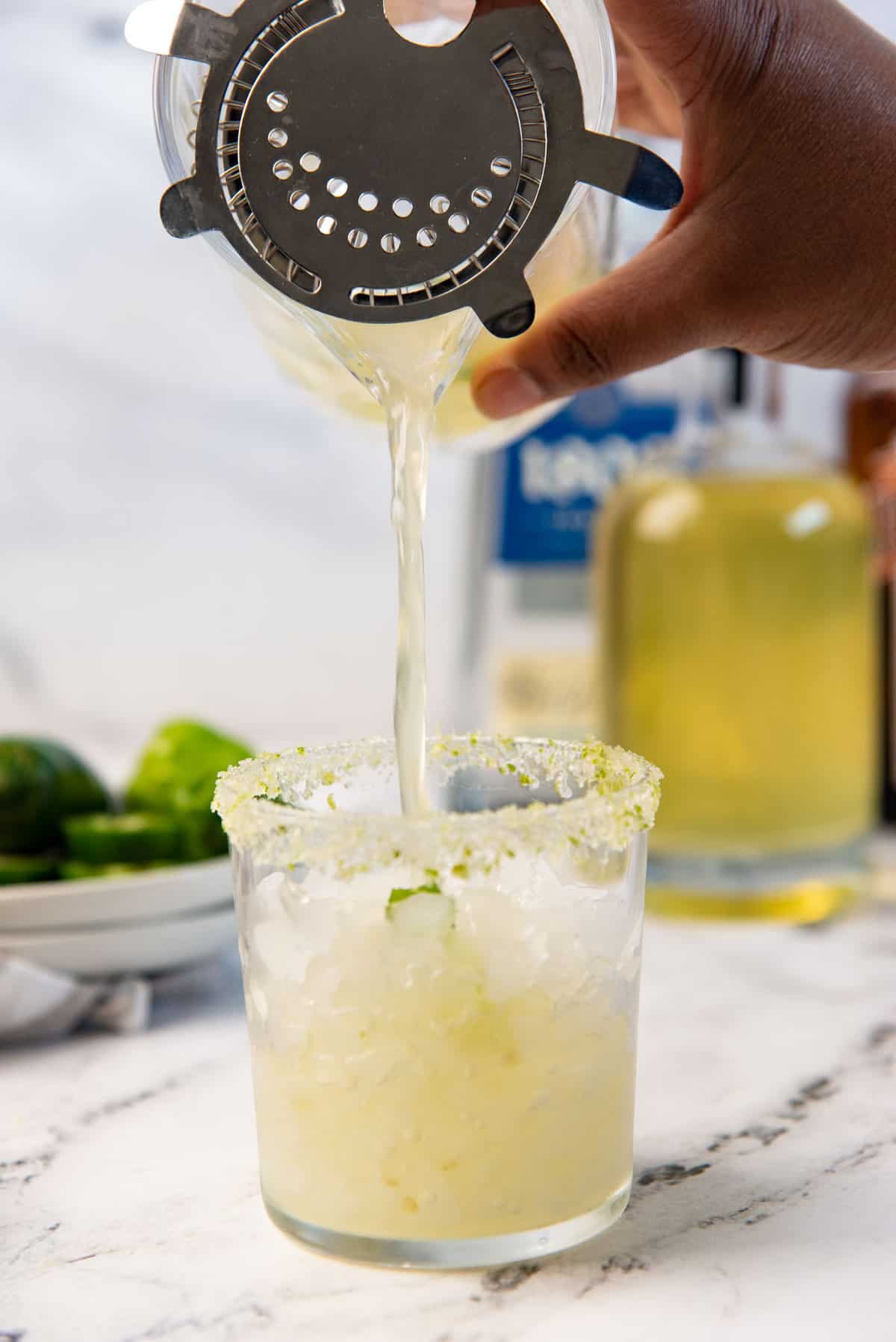 Pouring a margarita into a lime salt rimmed cocktail glass.