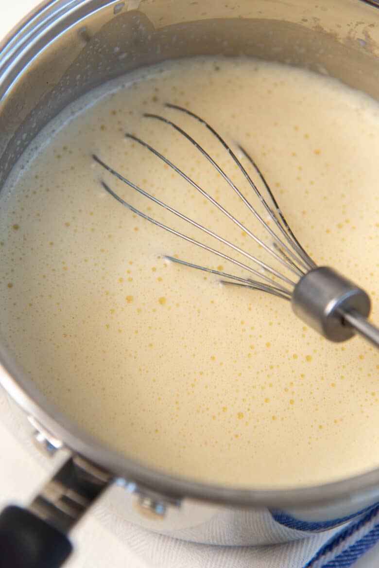 The banana milk and egg mixture in a saucepan with a whisk.