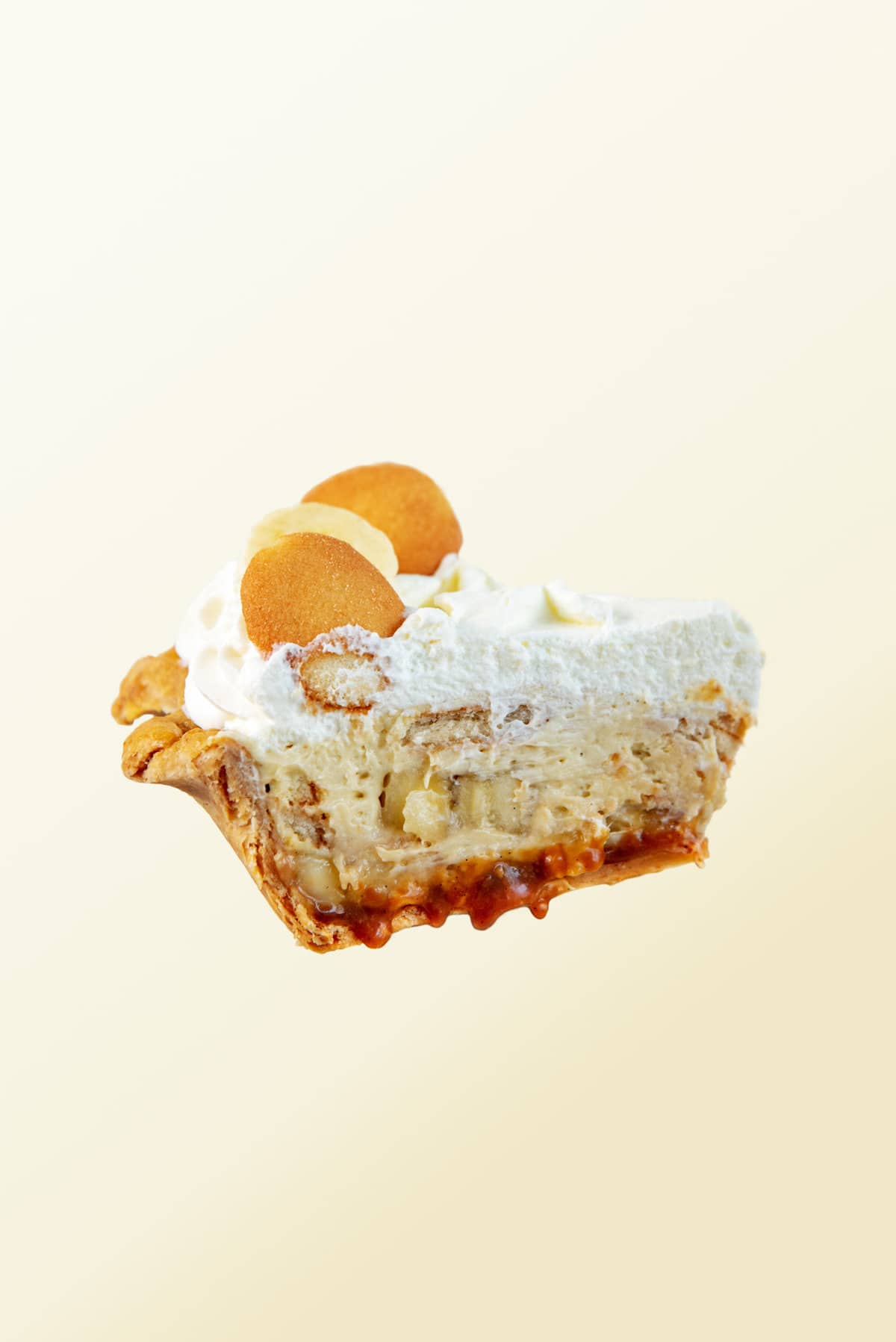 A slice of caramel banana cream pie slice "floating" with a yellow background. 