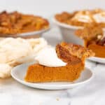 Slice of classic pumpkin pie with whipped cream served on a small plate.
