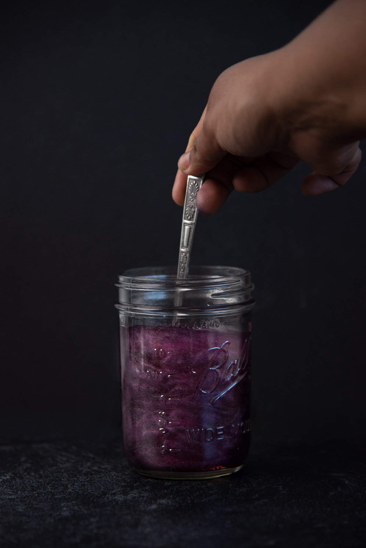 Blackberry flavored shimmery liqueur being stirred in a glass jar, showing the shimmery swirls.