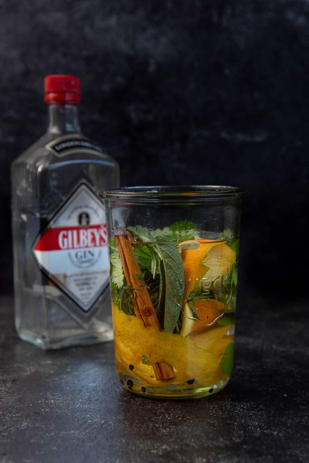 A tall weck jar filled with spices and herbs and gin.