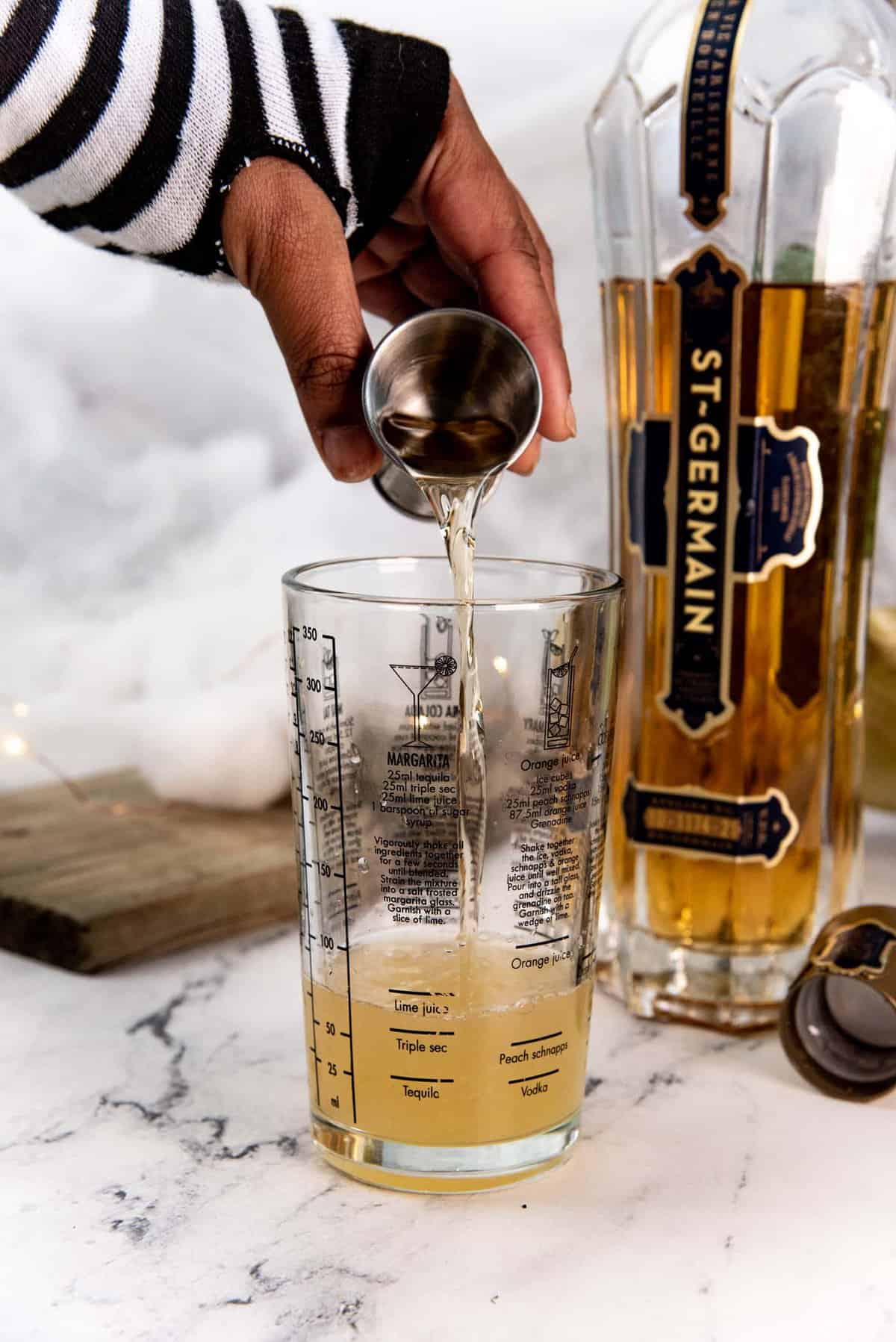 Pouring St Germain liqueur to the cocktail mixing glass, with the bottle in the background.