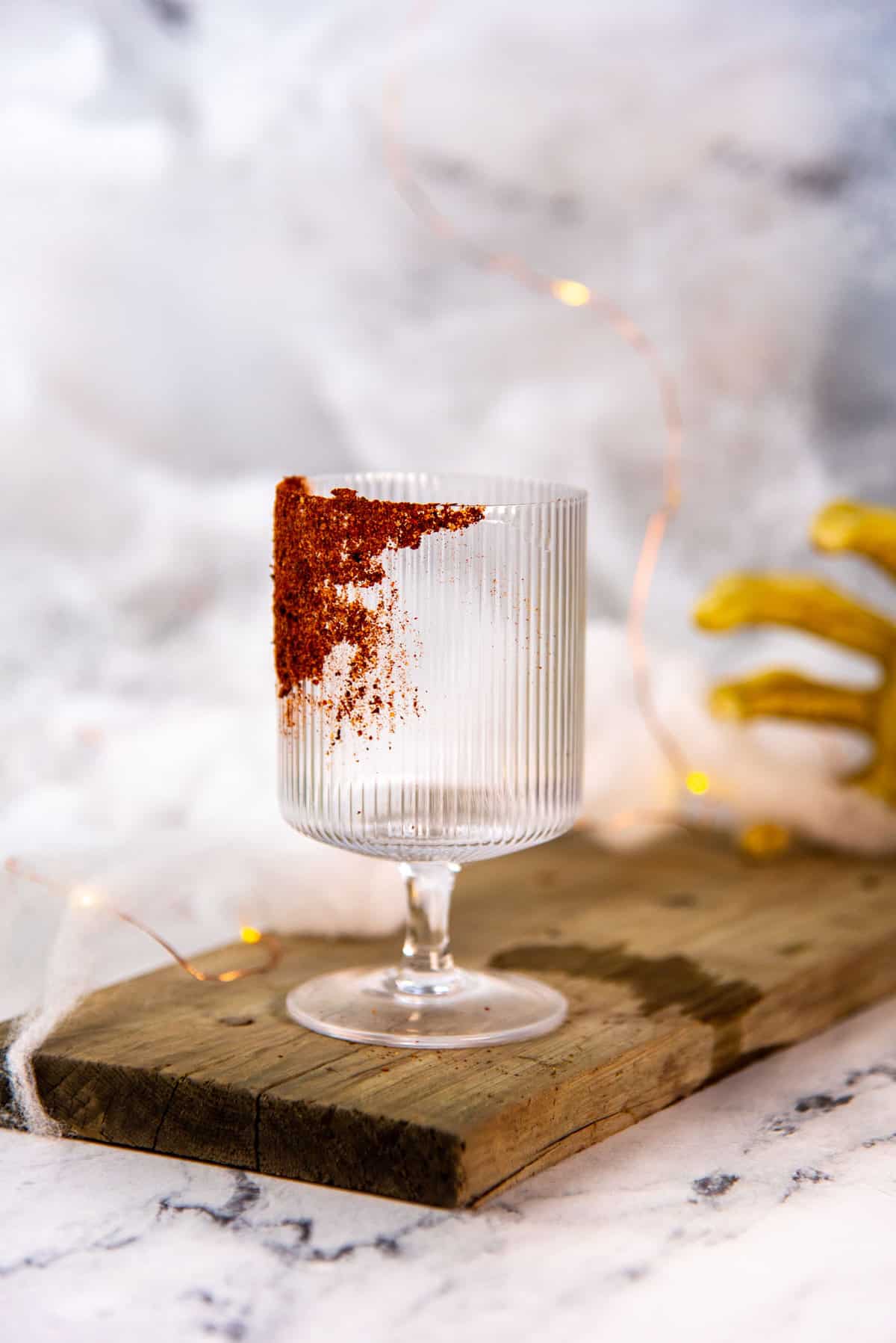 An empty goblet glass on a wooden board with the glass dipped in chili salt.