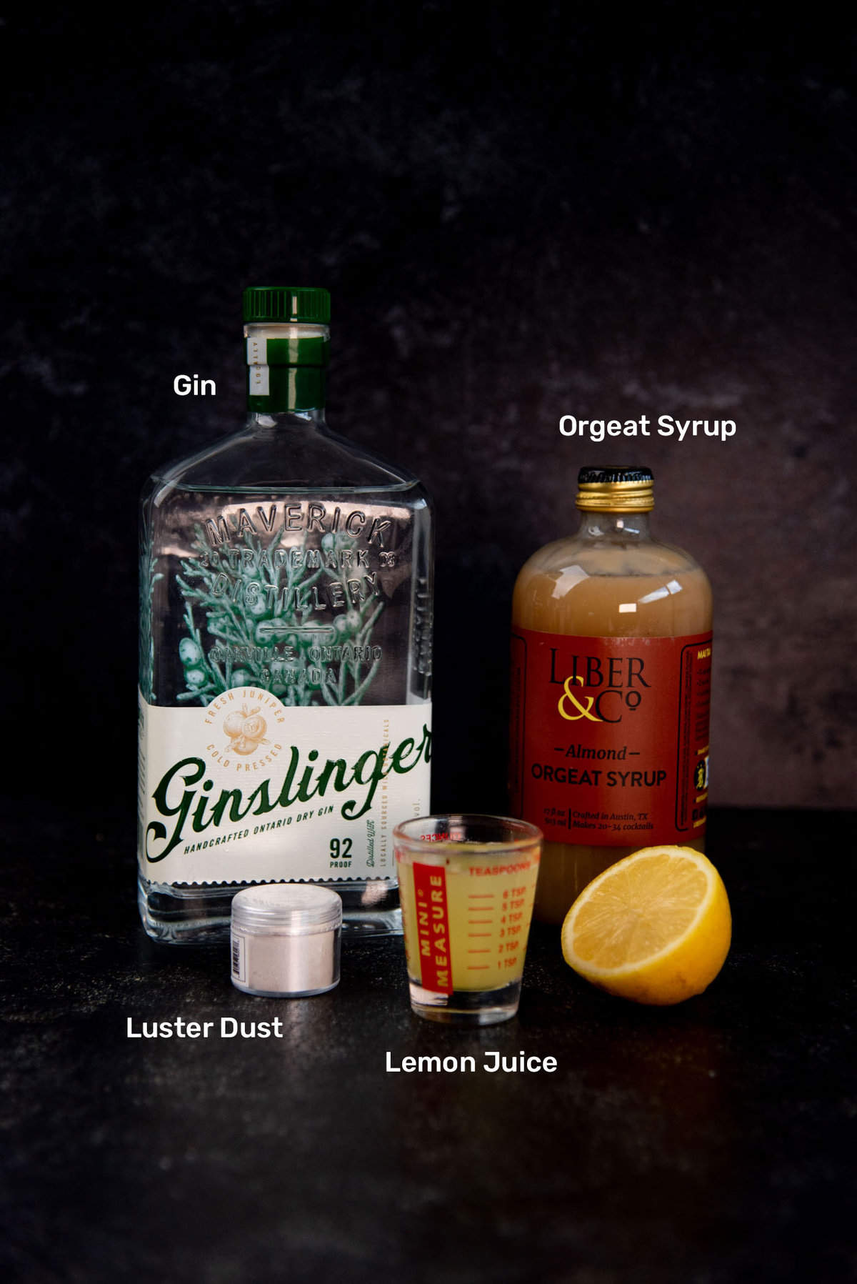 Ingredients to make Unicorn Blood Cocktail from left to right - Gin, Silver luster dust, lemon juice and orgeat syrup.