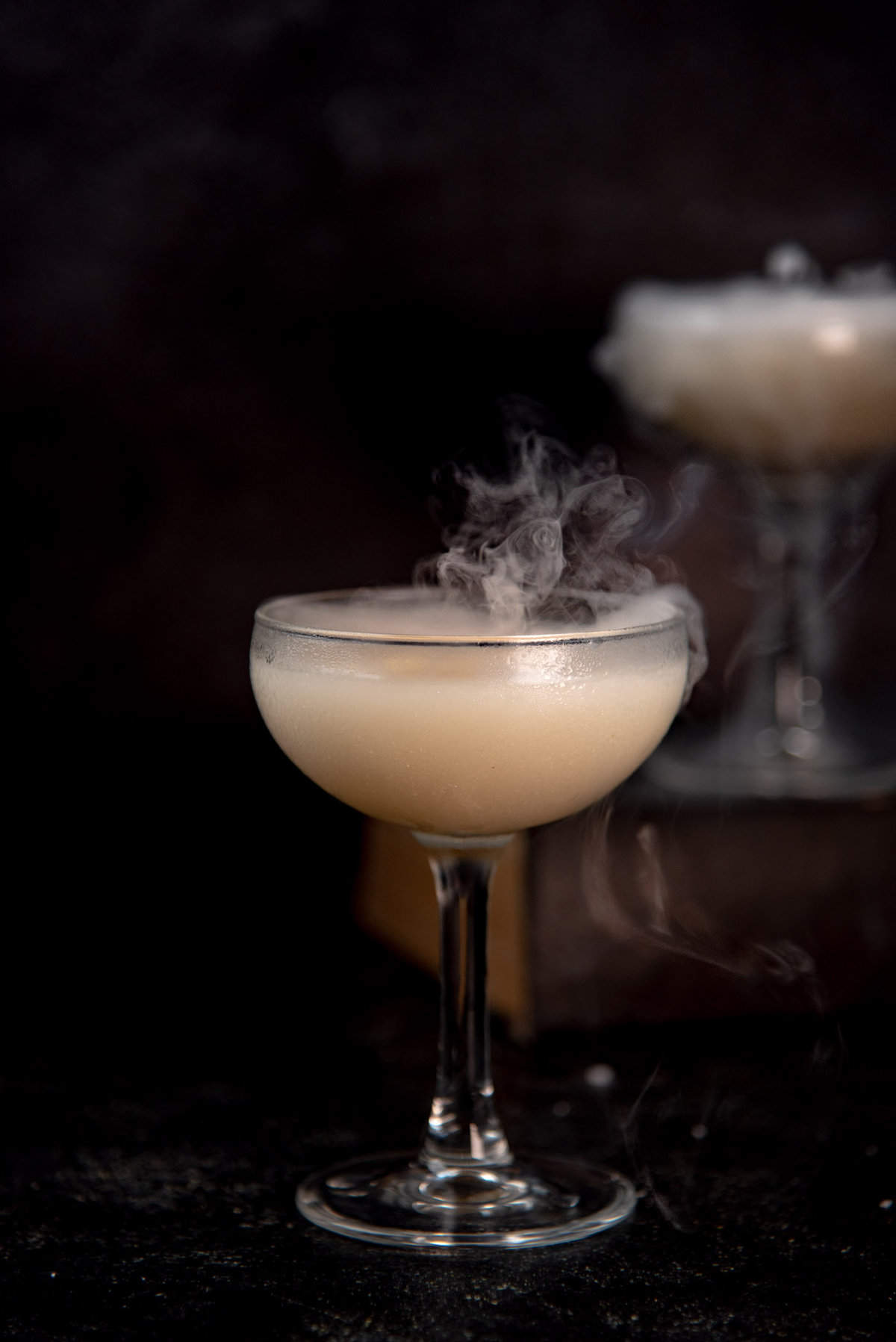 Harry Potter halloween cocktail that is shimmery white silver in color, with smoke coming out of the cocktail.