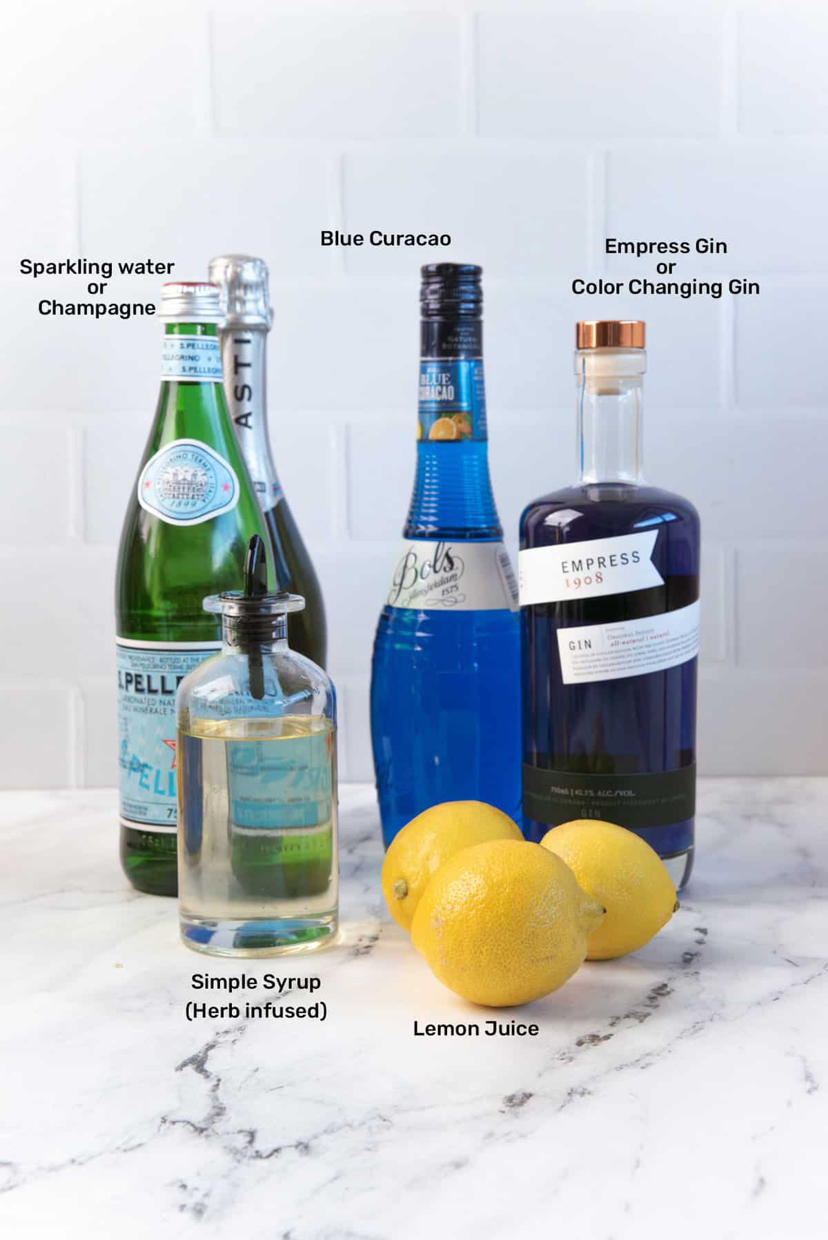 Ingredients to make the Witches brew drink, from empress gin, lemon juice, blue curacao, simple syrup, and sparkling water and water from right to left.