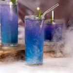 Witches Brew Halloween cocktail served in a glass with blue to purple color gradient with smoke in the background.