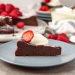 A slice of the flourless chocolate cake on a blue plate, topped with cream and strawberry slice.