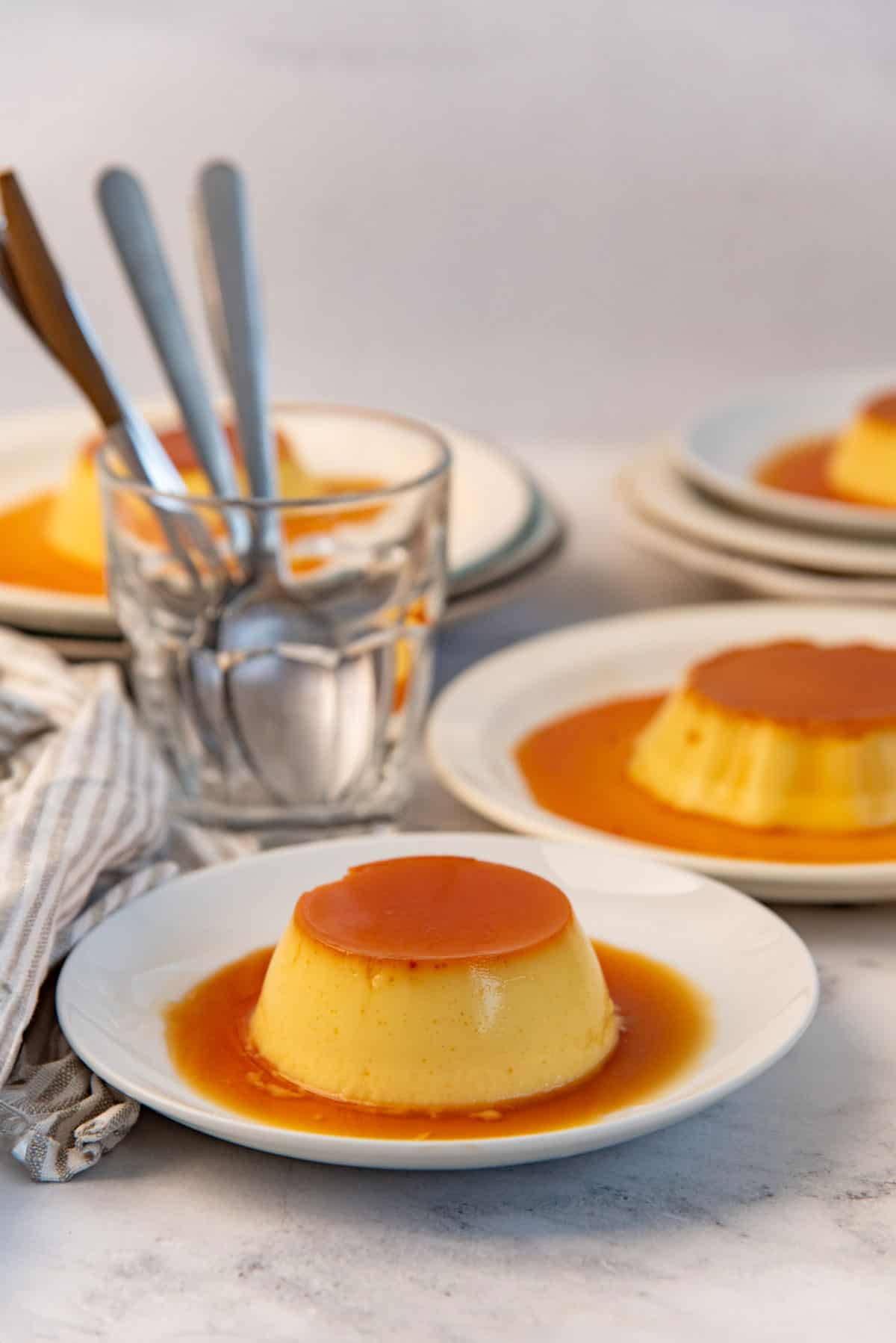 Plated cream caramel with other portions in the background and spoons.