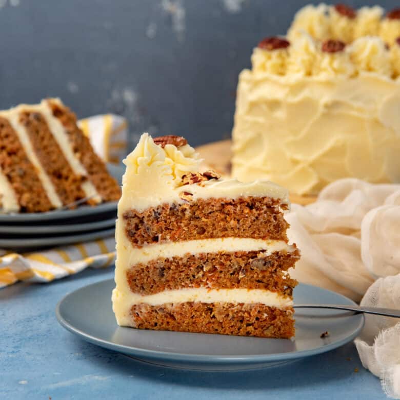 Slice of carrot cake with cream cheese frosting on a small blue platter.