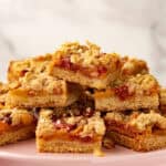 Stack of baked peach bars with crumble topping on a pink plate.