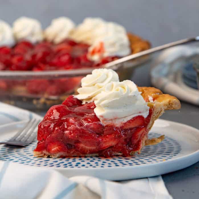 A fresh strawberry pie slice on a plate with whipped cream on top.
