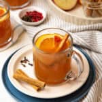 Spiced apple cider in a glass served with a garnish of cinnamon sticks.