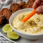 A carrot stick being dipped in the green curry yogurt dip that is served in a bowl.