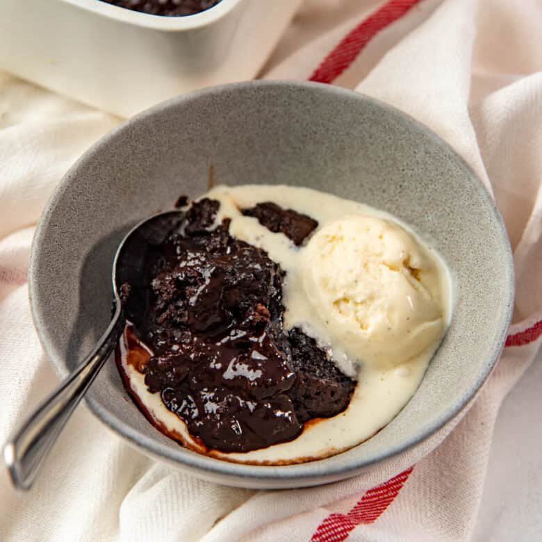 A fudgy piece of chocolate fudge pudding and the fudge sauce, served in a bowl.