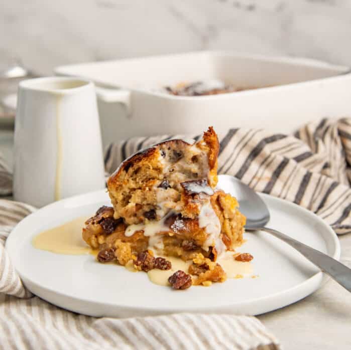 Close up of a serving of hot cross bun pudding with vanilla crème anglaise and a spoon.