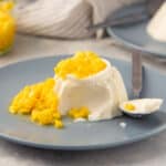 Buttermilk panna cotta topped with fresh mango and a bite taken out with a spoon.