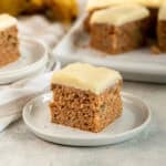 Old fashioned banana cake piece with cream cheese frosting served on a small white plate.