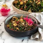 Tofu quinoa salad with peanuts and kale in a serving bowl with pickled onions and a spoon.