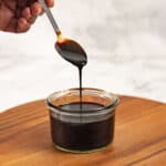 Picking up balsamic glaze with a spoon to show the dark color and thick consistency of the reduction.
