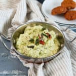 Green coconut chutney served in a small bowl with some dal vadai in the background.