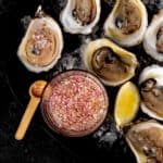 A platter of shucked fresh oysters on a bed of ice served with mignonette sauce.