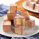 Coffee marshmallows on a plate with one half eaten to show coffee-colored fluffy interior.