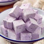 Close up of fluffy purple ube marshmallows stacked on a white plate.