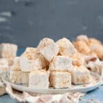 Stacks of toasted coconut marshmallows on a serving plate on a light blue surface.