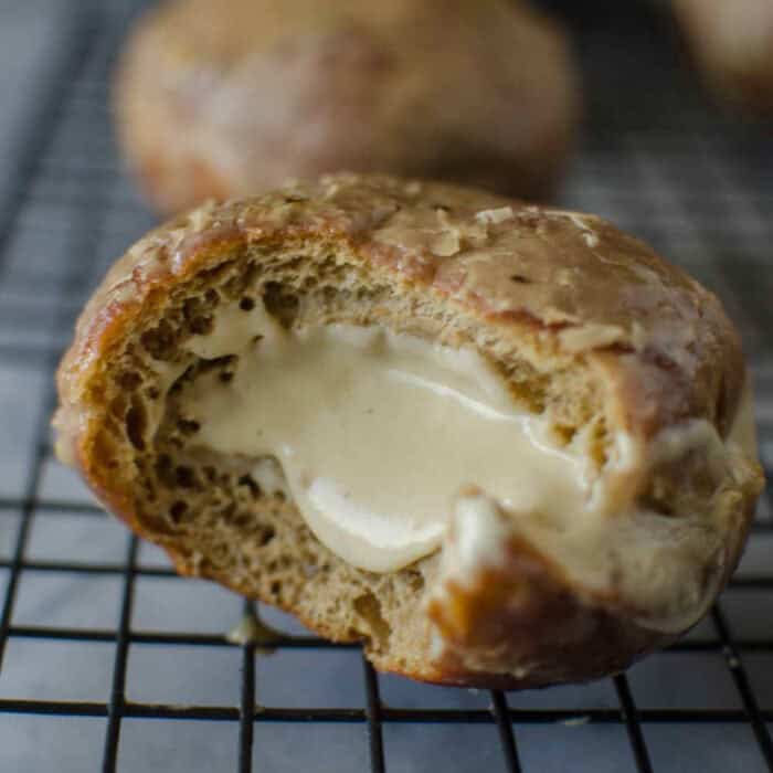 Half eaten coffee doughnut on a black wire rack showing the creamy white chocolate pastry cream filling inside.